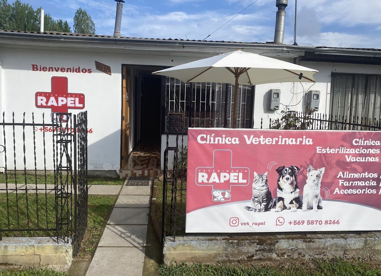 Fachada de Veterinaria Rapel en John Kennedy 514, Las Cabras: letrero rojo en el muro y lienzo rosa de servicios junto a la reja.